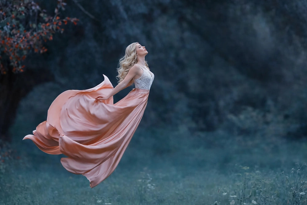 Woman in a flowing dress standing in a dark forest