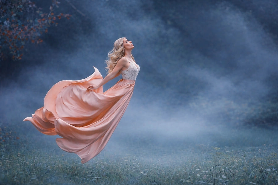 Woman in a flowing dress standing in a misty field with a dark blue sky.